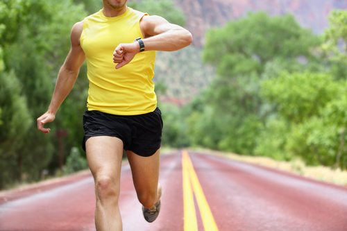 Runner with heart rate monitor sports watch. Man running looking at his pulse outside in nature on road.
